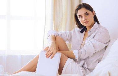 Sabahları yatakta otururken tablet kullanan ve kahve içen kadın portresi