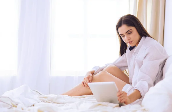 Ritratto di donna che usa tablet e beve caffè seduta sul letto al mattino — Foto Stock
