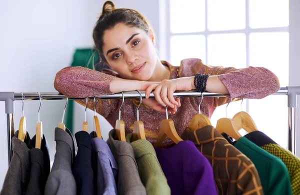 Schöne junge Stylistin in der Nähe von Gestell mit Kleiderbügeln — Stockfoto