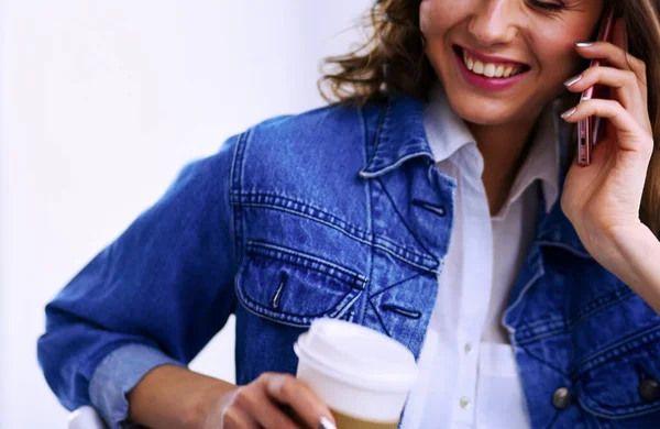 Kafede kahve içip cep telefonuyla konuşan genç bir kadın.