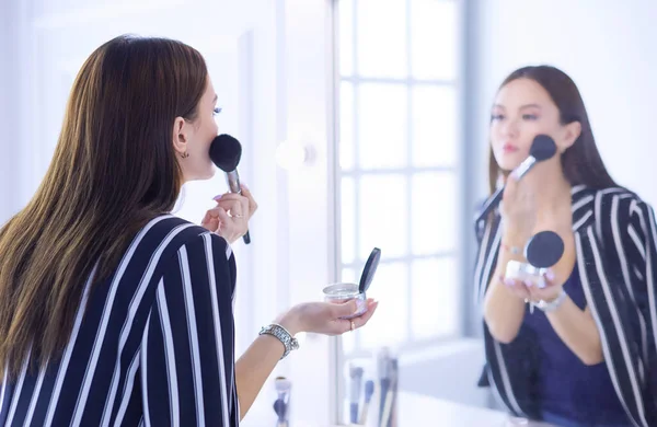 Beauty woman applying makeup. Beautiful girl looking in the mirror and applying cosmetic with a big brush — Stock Photo, Image