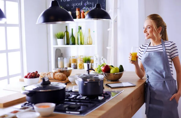Atractiva mujer sosteniendo un vaso de jugo de naranja mientras está de pie en la cocina —  Fotos de Stock