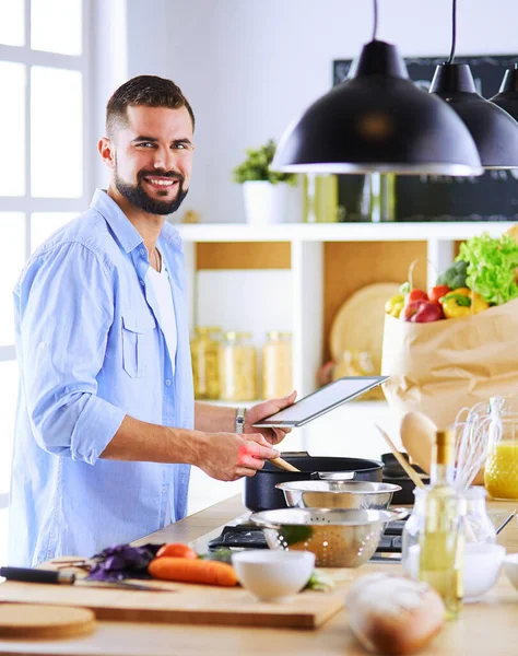 Hombre siguiendo la receta en la tableta digital y cocinar comida sabrosa y saludable en la cocina en casa —  Fotos de Stock