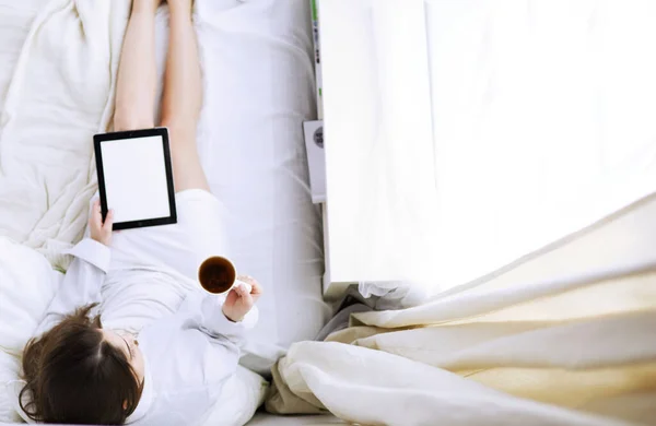 Porträt einer Frau, die morgens auf dem Bett sitzt und Tablette nimmt und Kaffee trinkt — Stockfoto