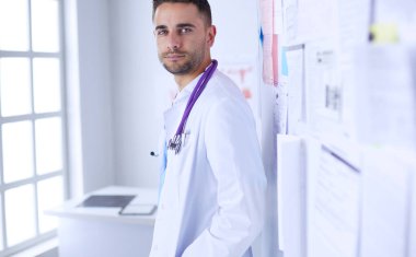 Genç ve kendinden emin erkek doktor portresi tıp ofisinde duruyor..