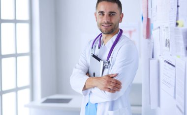 Genç ve kendinden emin erkek doktor portresi tıp ofisinde duruyor..