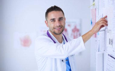 Genç ve kendinden emin erkek doktor portresi tıp ofisinde duruyor..