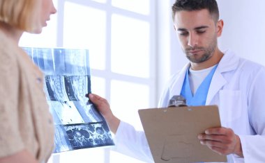 Yakışıklı doktor genç bayan hastasıyla konuşuyor ve ofisinde otururken notlar alıyor..