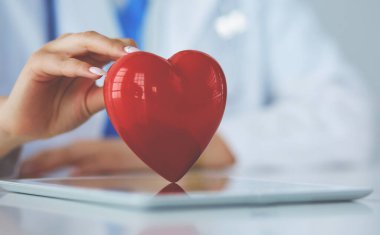 Steteskop tutan, kalbi hafif arka planda olan kadın bir doktor.