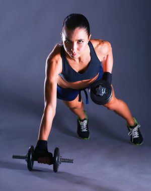 Dambıllarla egzersiz yapan genç bir kadın.