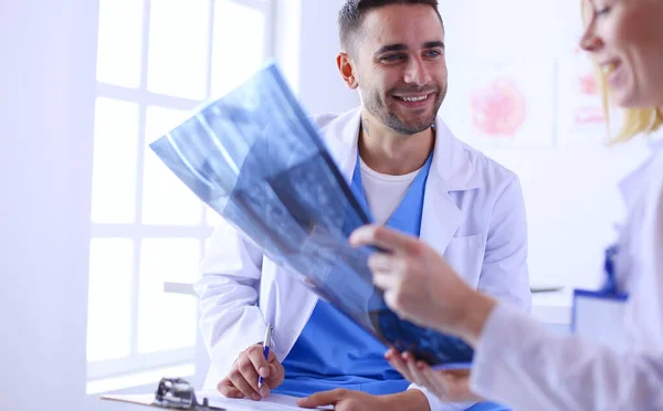 Schöner Arzt spricht mit junger Ärztin und macht sich Notizen, während er in seinem Büro sitzt. — Stockfoto