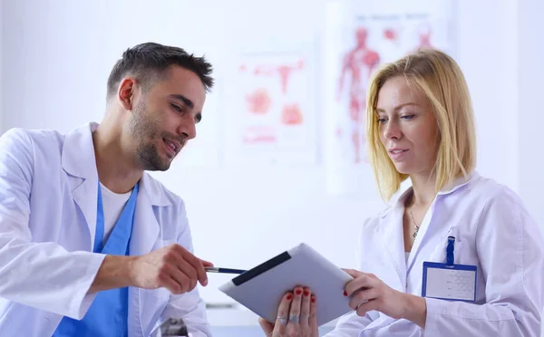 Bello medico sta parlando con giovane medico femminile e prendere appunti mentre seduto nel suo ufficio. — Foto Stock