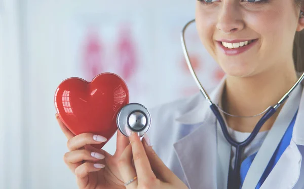 A doctor with stethoscope examining red heart, isolated on white — Stock Photo, Image