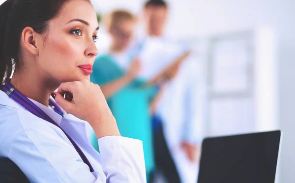 Bonito jovem sorridente médico feminino sentado na mesa — Fotografia de Stock