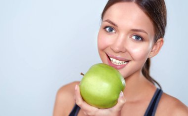 Mutlu genç kadın elma yiyor, beyaz arka planda soyutlanmış.