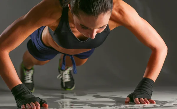 Mujer joven haciendo flexiones en una alfombra. — Foto de Stock