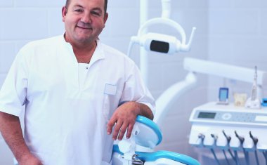 Diş kliniğinde duran gülümseyen bir dişçinin portresi.