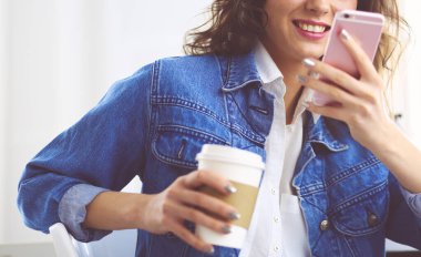 Kafede kahve içip cep telefonuyla konuşan genç bir kadın.