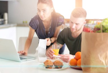 Sebze doğrayan genç bir adam ve mutfakta dizüstü bilgisayarı olan bir kadın.