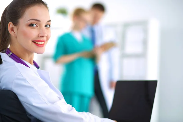 Vacker ung leende kvinnlig läkare sitter vid skrivbordet — Stockfoto
