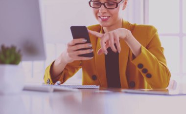 Dizüstü bilgisayarın önünde otururken cep telefonu ve mesaj kullanan bir iş kadınının portresi