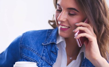 Kafede kahve içip cep telefonuyla konuşan genç bir kadın.