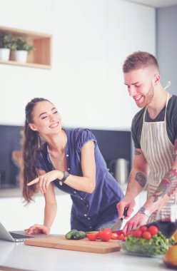 Sebze doğrayan genç bir adam ve mutfakta dizüstü bilgisayarı olan bir kadın.