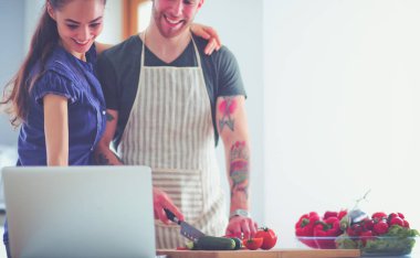 Sebze doğrayan genç bir adam ve mutfakta dizüstü bilgisayarı olan bir kadın.