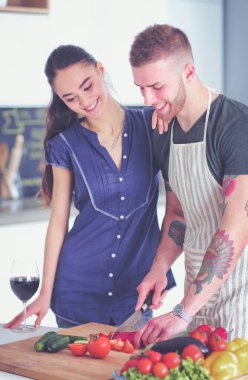 Sebze doğrayan genç bir adam ve mutfakta dizüstü bilgisayarı olan bir kadın.