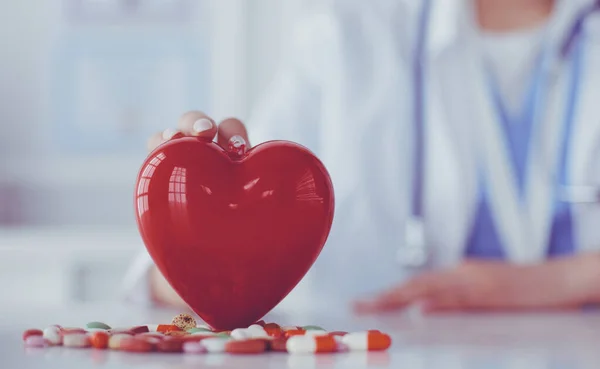 Médecin en manteau blanc avec stéthoscope tenant des pilules et coeur en plastique isolé sur blanc — Photo