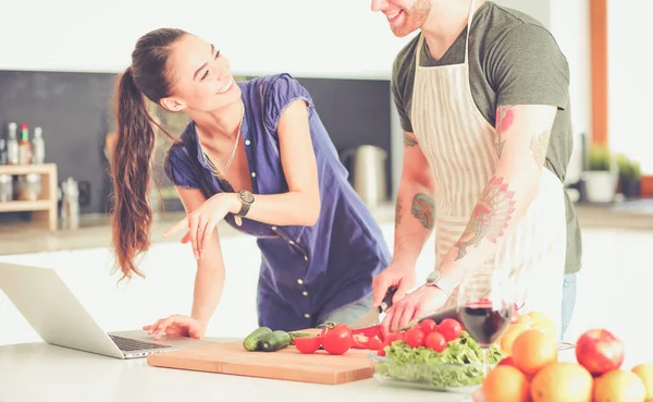 Sebze doğrayan genç bir adam ve mutfakta dizüstü bilgisayarı olan bir kadın.