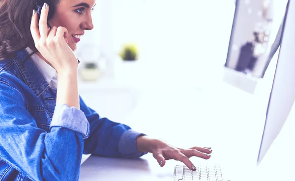 Heureuse charmante jeune femme assise et travaillant avec un ordinateur portable en utilisant un casque dans le bureau — Photo