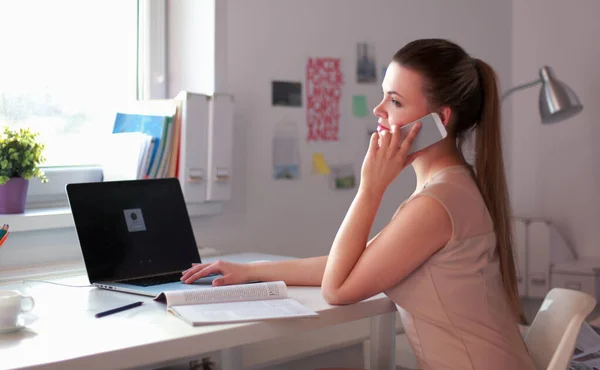 Jovem empresária sentada na mesa e conversando ao telefone — Fotografia de Stock