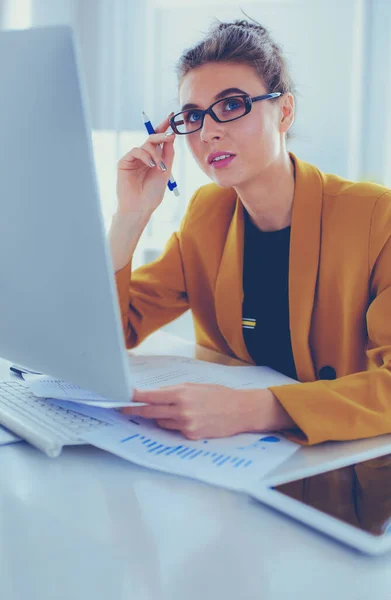 Hermosa joven mujer de negocios haciendo un poco de papeleo mientras está sentado en el escritorio de la oficina delante de la computadora portátil — Foto de Stock