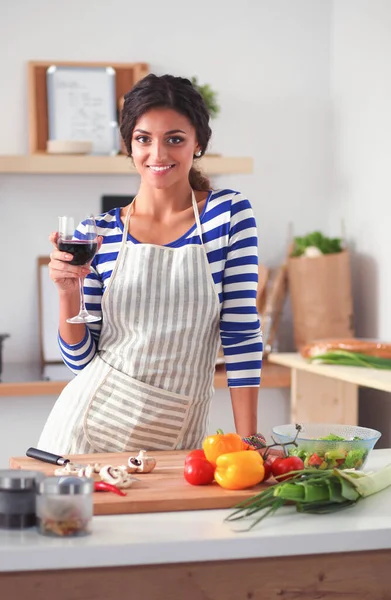 Jeune femme coupant des légumes dans la cuisine, tenant un verre de vin — Photo