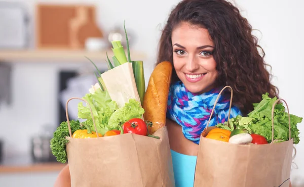 Mujer joven sosteniendo bolsa de la compra de comestibles con verduras de pie en la cocina. — Foto de Stock