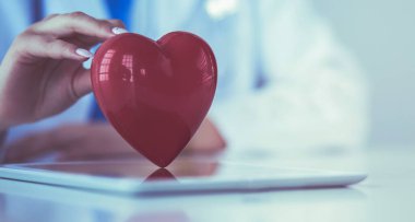 Steteskop tutan, kalbi hafif arka planda olan kadın bir doktor.