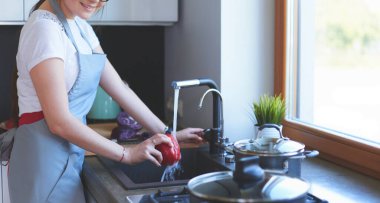 Sebze yıkayan kadın. Güzel genç bir kadın salata için sebze yıkıyor ve mutfakta dururken gülümsüyor.