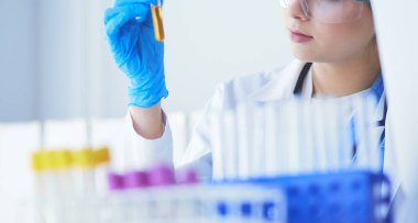 Bir kadın tıbbi veya bilimsel araştırmacı ya da kadın doktor laboratuarda bir test tüpü dolusu temiz çözeltiye bakıyor.