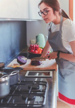 Mutfakta yemek yapmak için tablet bilgisayar kullanan genç bir kadın.