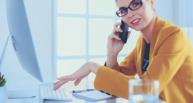 İş kadını ofiste bilgisayar ve cep telefonu kullanarak işine konsantre oluyor.