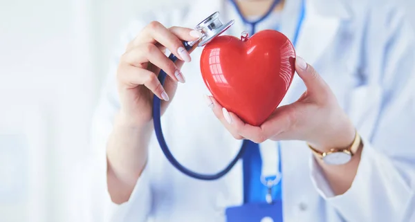 Steteskoplu bir doktor, beyaz arka planda kırmızı kalbi inceliyor. — Stok fotoğraf
