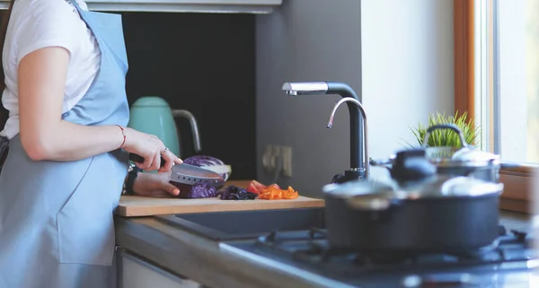 Молодая женщина режет овощи на кухне стоя возле стола — стоковое фото