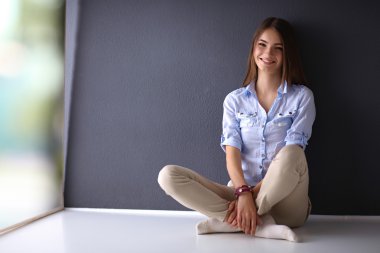 Genç bir kadın yerde, kara duvarın yanında oturuyor.