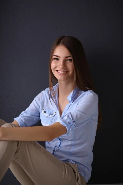 Jonge vrouw zittend op de vloer geïsoleerd donkere achtergrond — Stockfoto