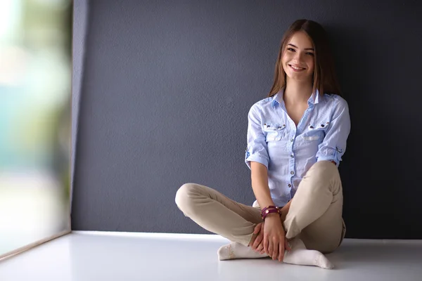 Jonge vrouw zit op de vloer in de buurt van donkere muur — Stockfoto