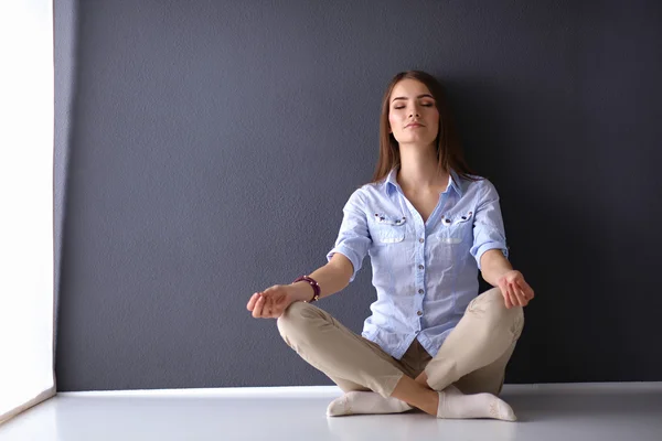 Jovem mulher sentada no chão perto da parede, fazendo ioga — Fotografia de Stock