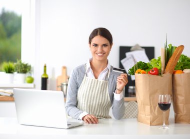 Mutfakta bilgisayar ve kredi kartı kullanan gülümseyen bir kadın.