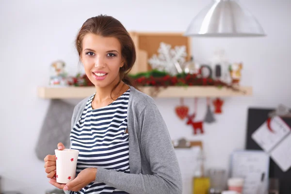 Portrett av en ung kvinne med kopp mot kjøkkenets indre bakgrunn. – stockfoto