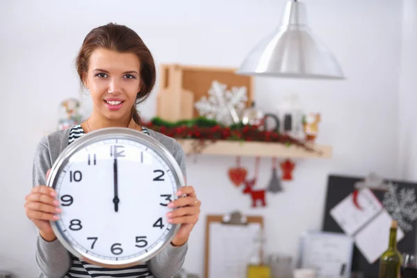 Wanita muda yang bahagia yang menunjukkan jam di dapur Natal dengan dekorasi — Stok Foto